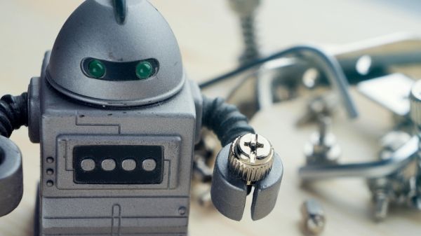 A robot toy holding a screw with various metal parts blurred behind it