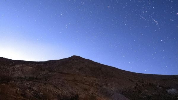 A night sky with stars and a hill in front of it