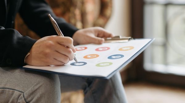 Up-close of a clipboard with paper that has icons on it, being marked by a pen.