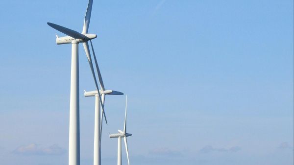 Three wind turbines lined up in a green field with a blue sky behind them