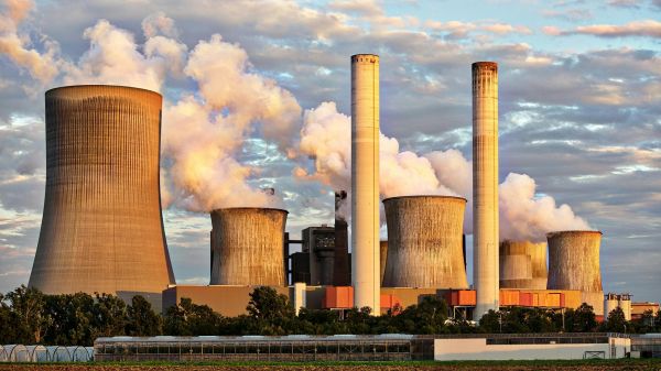 A factory with a number of smokestacks in front of a blue cloudy sky