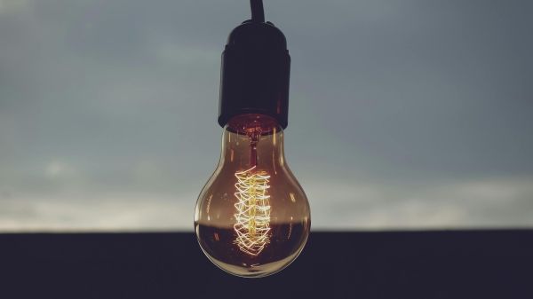 A lightbulb hanging from the ceiling in front of a window with a blurred city skyline.