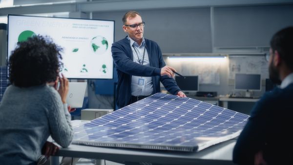 NNOCCI Climate Change Communication Training Three people are arranged around a solar panel; one person is standing and holding part of the panel with a presentation board behind them