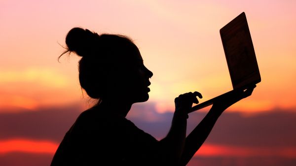 woman holding computer outside at sunset