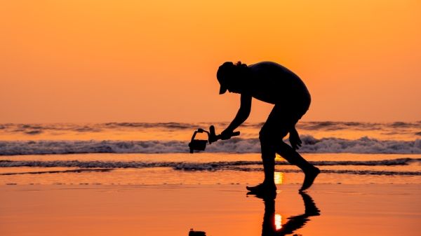 An image of a man on a beach at sunset filming with a handheld camera