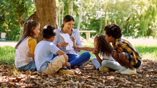 an educator sits in a circle with young kids outside