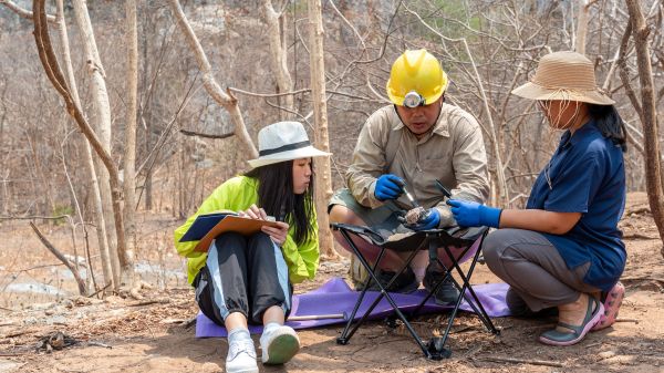 Three scientists in the field examining a rock sample.