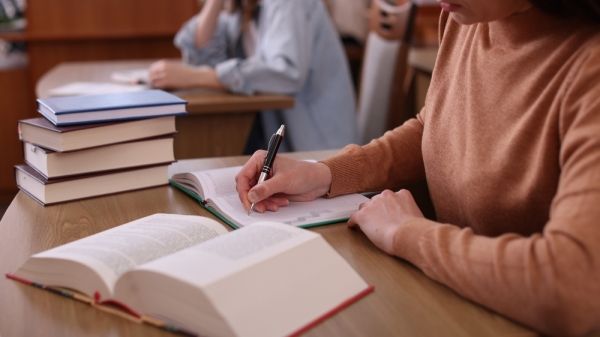 Students sit at desks with book stacks.