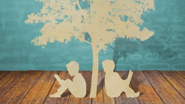 paper cutouts of two students reading under tree, sitting on brown wood floor in front of suggested painted blue bricks