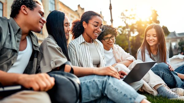 students sitting on grass on campus socializing, studying and spending time at leisure. 