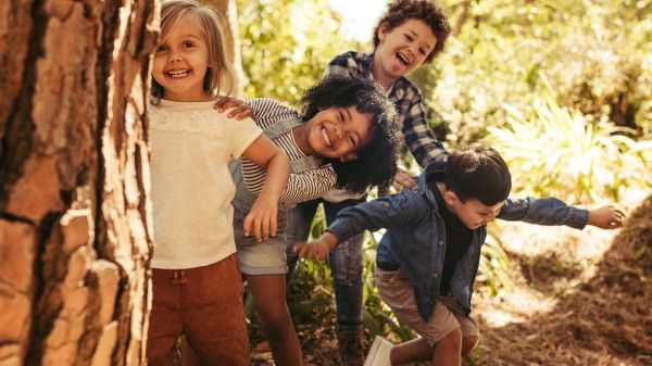 Young children peek behind a tree during autumn