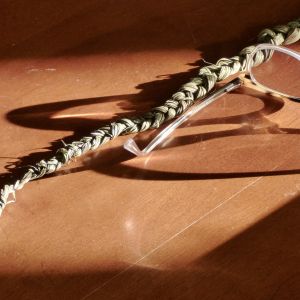 A strand of braided sweetgrass and a pair of glasses rest on a table with the sun created shadows across them. Photo credit:Judith Jackson