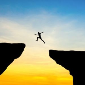 Person leaping over a chasm at sunset