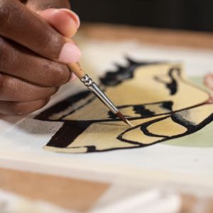 Close-up of a Black artist painting a butterfly on paper