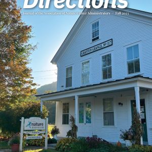 Cover of Directions, featuring a white A-frame building. Behind the building the sun shines. To the left is an autumnal tree with orange, yellow, and green leaves.