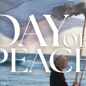 Jane Goodall holds a giant peace dove puppet near the ocean. DAY OF PEACE is written over the image.
