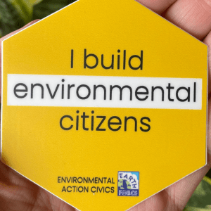 A hand holds a yellow pin that says "I build environmental citizens." Earth Force logo is at the bottom.