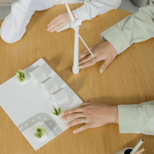 Two people sit at a table with a paper town and miniature wind turbine