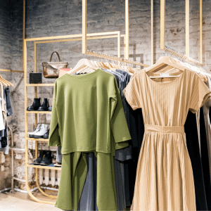 A brick-walled room contains a shelf of shoes, rack of clothes, a shelf of shoes and a handbag, and an additional rack of clothes