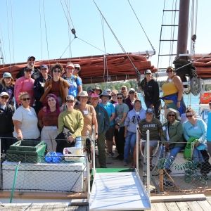 A group of teachers smile while sitting on the deck of a tall ship schooner.