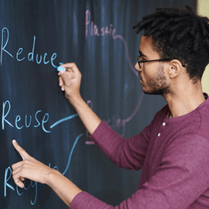 A person writes "Reduce, Reuse, Recycle" in blue chalk on a chalkboard to the left of them; their left hand points to the word Reuse