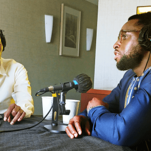 Ritchie Tusabe and Harrison Ashangwa sit at microphones and wearing headphones as they record their episode of The World We Want podcast