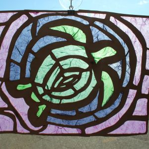 A tissue paper suncatcher depicting a green sea turtle in a blue circle on a purple background