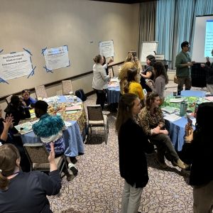 Photograph of several workshop participants interacting with each other in an indoor space with tables.