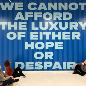 Course Facilitators sitting by a mural that reads 'We cannot afford the luxury of either hope or despair'