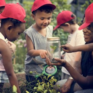 Kids outside looking at a glass jar held out by their teacher 