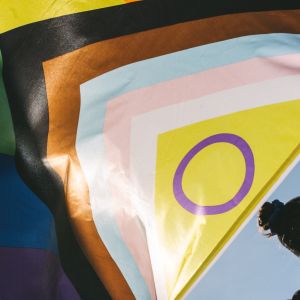 A person holds LGBTI+ flag behind them