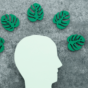 A cutout silhouette of a head in white is below five green leaf cutouts, all against a gray textured background
