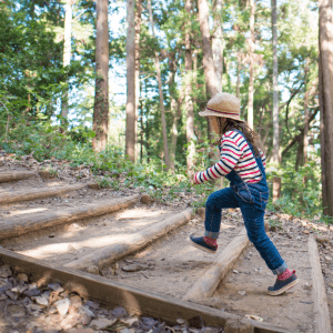 A child walks up a hill along some wood and dirt steps; behind them is a forested area with trees