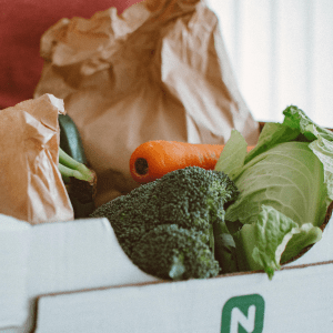 A person in a red shirt holds a cardboard box with vegetables