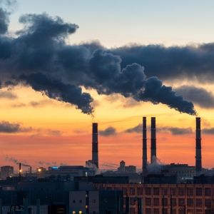 A sunsetting landscape with smoke rising out of factory buildings.