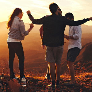 Four people facing away from the camera against a hilly sunset background