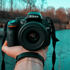 A hand holds out a camera facing the viewer, beyond it is a river