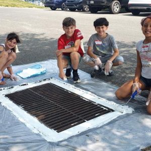 Four smiling students stencil a storm drain.