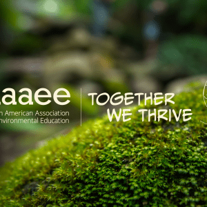 Background image is a close-up of a mossy rock with white text and illustration in the foreground that reads, "NAAEE. Together We Thrive," and an outline of a pair of hands holding a 2D outline of the world