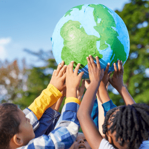 A group of children hold up a paper mache globe above their heads; behind them is a partly cloudy sky and a blurred green tree