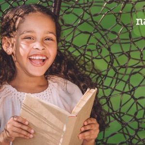 green background with little girl smiling in forefront with a book in hands