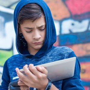 Young person in blue hoodie looking at tablet.
