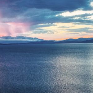 Overlooking large body of dark blue water with heavy blue, purple, and pink clouds in the distance.