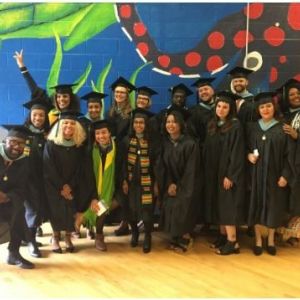 group of graduates in black robes and caps in front of colorful mural