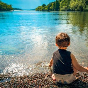 A toddler sits by the edge of a lake
