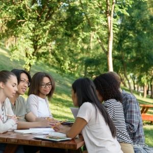 Image of multiethnic group of young students sitting and studying outdoors while talking.