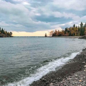 A rocky lakeshore lined by trees in autumn
