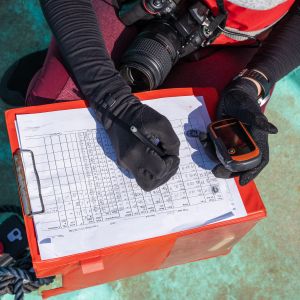 Top view of an unrecognizable marine biologist writing data on a paper on a boat