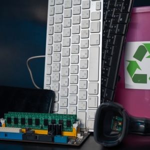 A keyboard, phone, headphones, and other electronics sit next to a recycle sign.