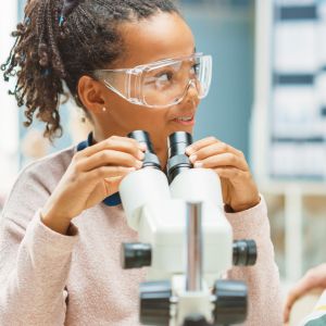 A girl looking away from a microscope and on the left, a boy looking at a digital tablet